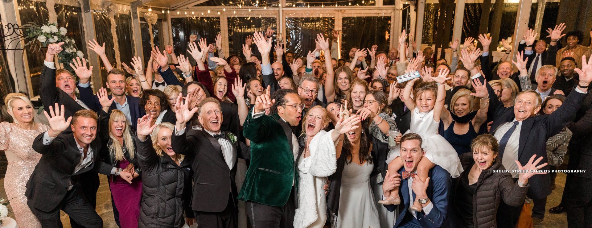 Group of people celebrating at a wedding reception with hands in the air and big smiles on their faces