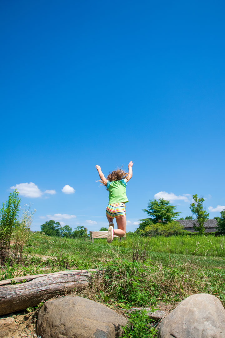 A young girl leaps off a stone into the blue sky